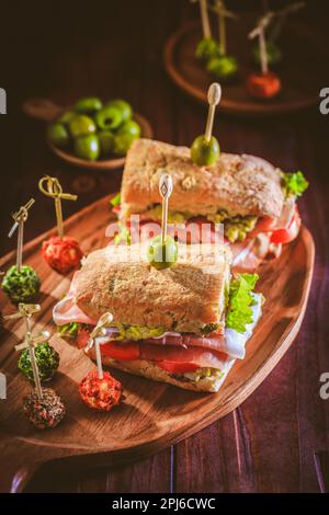 Homemade Ciabatta sandwich with guacamole, prosciutto, lettuce, tomato and olives Stock Photo