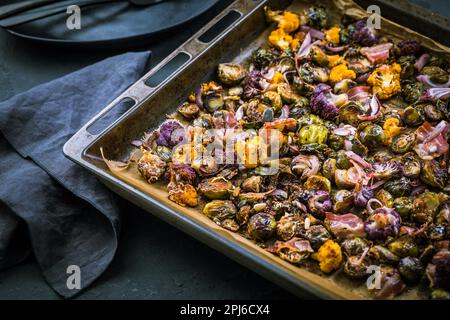 Healthy food - Baked vegetables with Purple Brussels sprouts, broccoli, cauliflower and onions on baking sheet Stock Photo