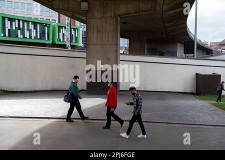 People pass by underneath the elevated section of the A38 Aston Expressway on 22nd March 2023 in Birmingham, United Kingdom. The A38M, commonly known as the Aston Expressway, is a motorway in Birmingham, England. It is 2 miles long and was opened on 24 May 1972. It connects the M6 motorway to Aston and Central Birmingham and forms part of the much longer A38 route. Stock Photo