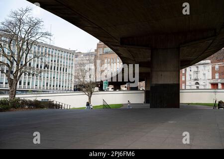 People pass by underneath the elevated section of the A38 Aston Expressway on 22nd March 2023 in Birmingham, United Kingdom. The A38M, commonly known as the Aston Expressway, is a motorway in Birmingham, England. It is 2 miles long and was opened on 24 May 1972. It connects the M6 motorway to Aston and Central Birmingham and forms part of the much longer A38 route. Stock Photo
