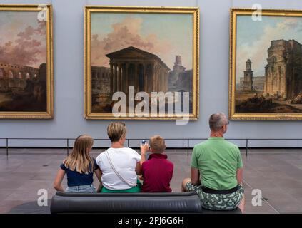 A man, a woman and two children, with their backs to the photographer, look at a painting on a wall in the Louvre, Paris, France Stock Photo