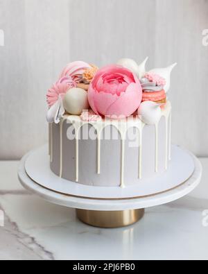 Beautiful and elegant grey cake decorated with melted white chocolate, macaroons, pink peony flower, cake pops and candies on marble cakestand Stock Photo