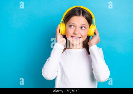 Photo of optimistic satisfied girl wear white long sleeve look empty space arms touching headphones isolated on blue color background Stock Photo
