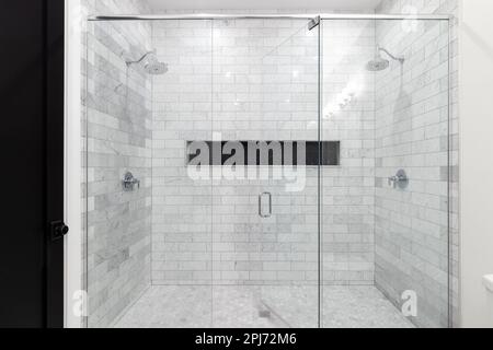 A large, luxury double shower with marble subway tile walls, marble hexagon floor, and a tiled shelf with small black hexagon tiles. Stock Photo