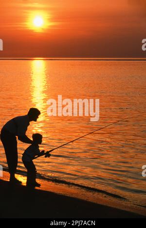 Father and young son fishing together in the Atlantic ocean at sunset Stock Photo