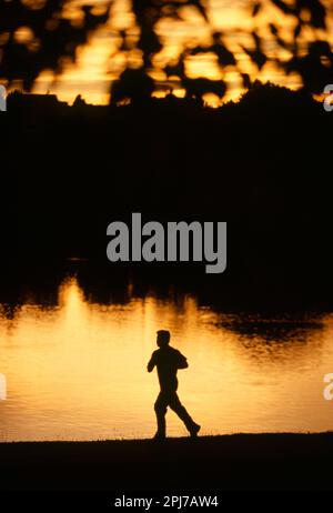 A silhouette of a man jogging alone a leak at sunset Stock Photo