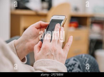 An elderly woman holds and uses a smartphone in her hand, a smartphone. Grandmother. Close-up, the concept of family connections Stock Photo