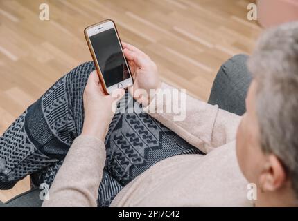 An elderly woman holds and uses a smartphone in her hand, a smartphone. Grandmother. Close-up, the concept of family connections Stock Photo