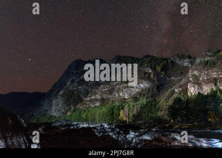 Stone bank of the Katun river at night near the illuminated mountain under the stars and the milky way in the Altai Stock Photo