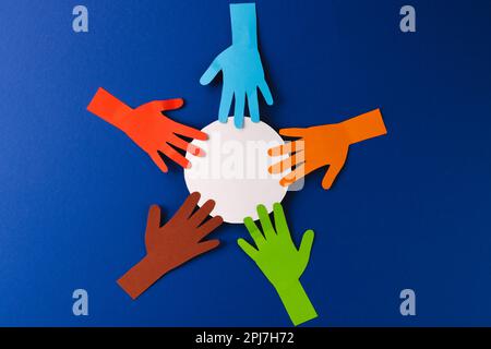 Paper cut out of multi coloured hands and white circle with copy space on blue background Stock Photo