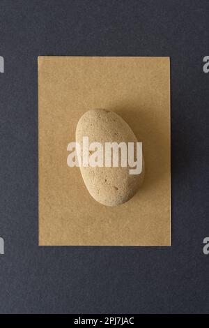 ovoid shaped brick pebble isolated on gold or sand brown card and grey paper Stock Photo