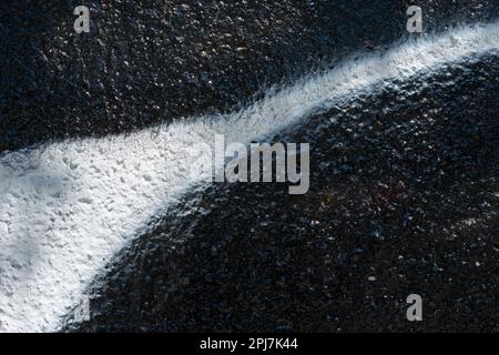 rough retaining wall painted with shiny black paint and a spray painted line Stock Photo