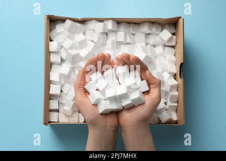 Woman holding heap of styrofoam cubes over box on light blue background, top view Stock Photo
