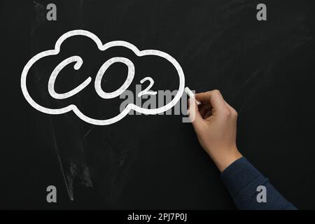 Reduce carbon emissions. Woman drawing cloud with chemical formula CO2 on blackboard, closeup Stock Photo