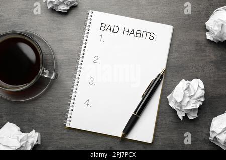 Notebook with list of bad habits, pen, crumpled paper balls and cup of coffee on grey table, flat lay. Change your lifestyle Stock Photo