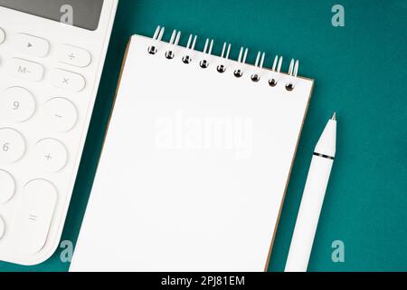 Blank Spiral notebook and pen with calculator on green background, top view, flat lay. Stock Photo