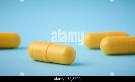 close-up of yellow gelatin capsules pills, oral medical drug filled with powder or liquid form on blue background, selective focus with copy space Stock Photo