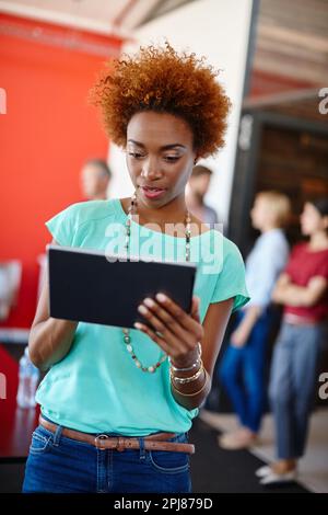 Focused on the task at hand. a young designer using a tablet with her colleagues standing in the background. Stock Photo