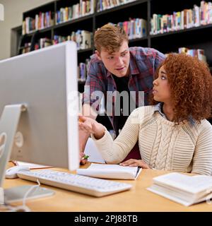 Collaborating on an assignment. two students working together at a computer in a university library. Stock Photo