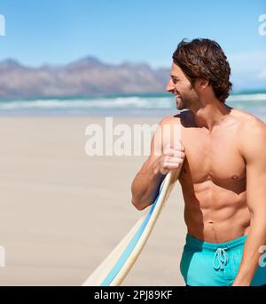 Surfing keeps him in great shape. A young man standing next to his surfboard looking around. Stock Photo