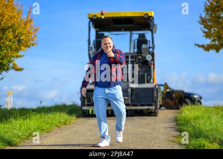 Young man with a commanding smile wearing a red and blue lumberjack jacket and blue t-shirt points to the camera and walks towards the camera with agr Stock Photo