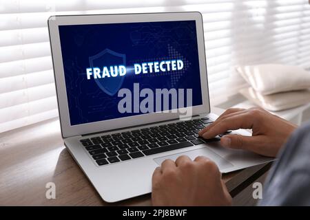 Fraud prevention security system. Man using laptop at wooden table, closeup Stock Photo