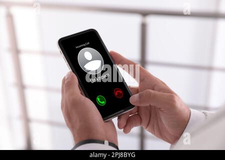 Man deciding answer incoming call from unknown caller or not indoors, closeup. Be careful - fraud Stock Photo