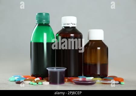 Bottles of cough syrup, dosing spoon, measuring cup and pills on light background Stock Photo