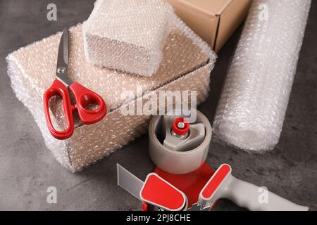 Cardboard boxes, bubble wrap, adhesive tape and scissors on dark grey table Stock Photo