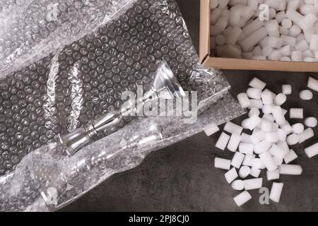Elegant silver candlesticks, bubble wrap and cardboard box with foam peanuts on dark grey table, flat lay Stock Photo
