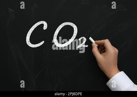 Reduce carbon emissions. Woman writing chemical formula CO2 on blackboard, closeup Stock Photo