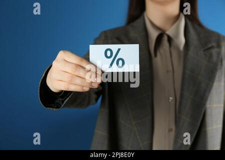 Woman showing business card with percent sign on blue background, closeup. Discount concept Stock Photo