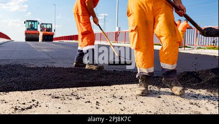 Few workers are using shovels to level, set up layer of fresh tarmac to right measures, pouring hot asphalt. Stock Photo