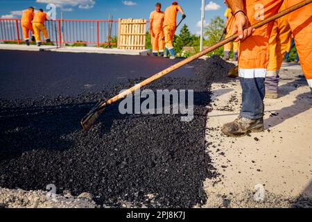 Few workers are using shovels to level, set up layer of fresh tarmac to right measures, pouring hot asphalt. Stock Photo