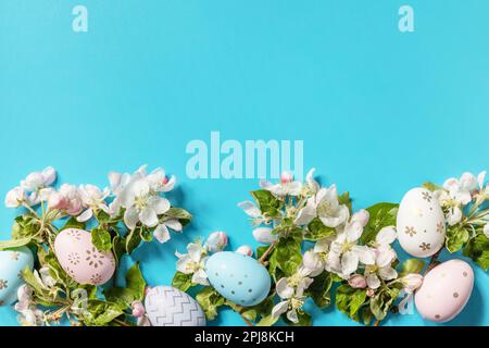 Easter composition with colorful eggs and flowers of apple tree on a blue background. Spring concept, flowers composition. Greeting card. View from ab Stock Photo