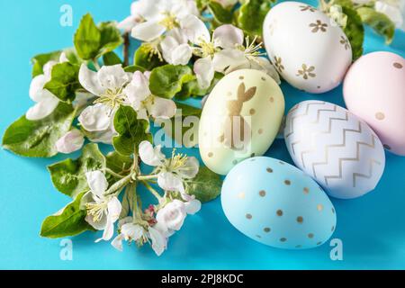 Easter composition with colorful eggs and flowers of apple tree on a blue background. Spring concept, flowers composition. Greeting card. Stock Photo