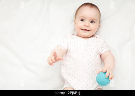 Cute baby girl playing with sensory ball on bed. Top view Stock Photo