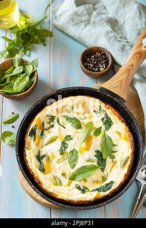 Healthy frittata or stuffed omelette in pan on rustic wooden background. Italian omelette with organic spinach and bell pepper. Stock Photo