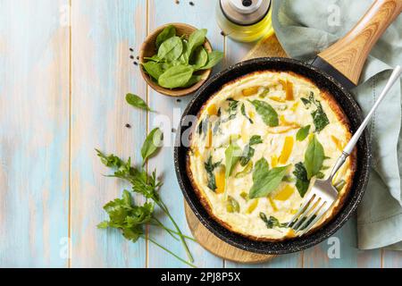 Healthy frittata or stuffed omelette in pan on rustic wooden background. Italian omelette with organic spinach and bell pepper. View from above. Copy Stock Photo