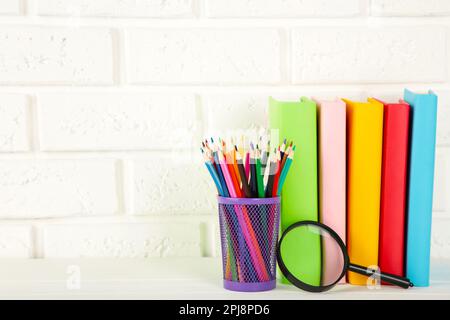 Multi coloured school books and stationery on white brick wall background. Copy space Stock Photo