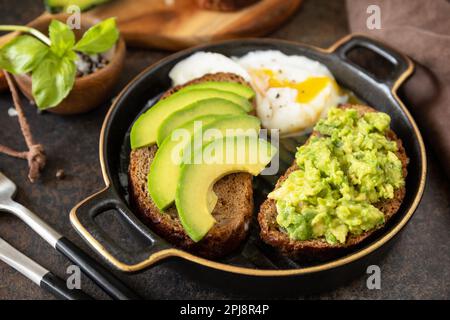 Healthy breakfast concept, sandwich with avocado and egg. Wholemeal bread toast sliced avocado and poached egg on a stone background. Stock Photo