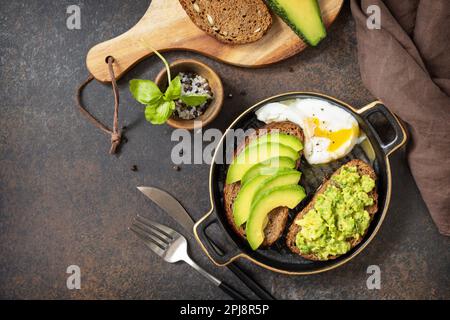 Healthy breakfast concept, sandwich with avocado and egg. Wholemeal bread toast sliced avocado and poached egg on a stone background. View from above. Stock Photo