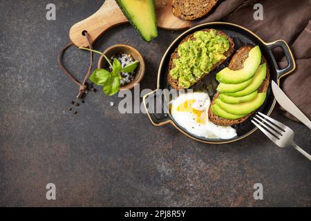 Healthy breakfast concept, sandwich with avocado and egg. Wholemeal bread toast sliced avocado and poached egg on a stone background. View from above. Stock Photo