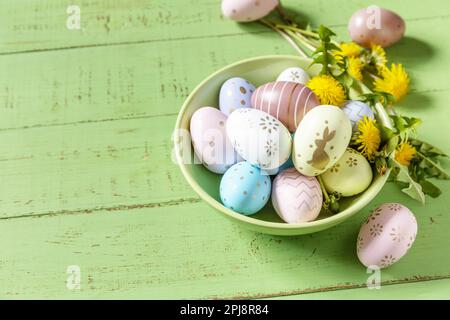 Happy Easter Holidays. Handmade Easter colorful eggs and spring flowers dandelions on a rustic wooden table. Easter composition. Copy space. Stock Photo