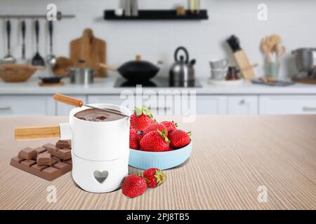 Fondue pot with chocolate and fresh strawberries on wooden table in kitchen. Space for text Stock Photo
