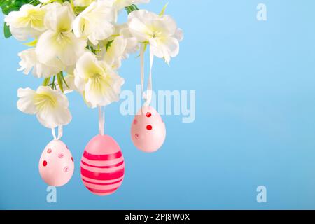 Delightful Easter banner of pink easter eggs suspended from a blooming branch against a calming blue background Stock Photo