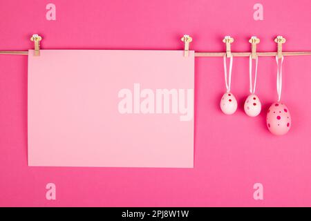 Blank pastel pink sheet of paper and three pink Easter eggs hang at rope on vibrant pink background. Easter card design with open area for personalize Stock Photo
