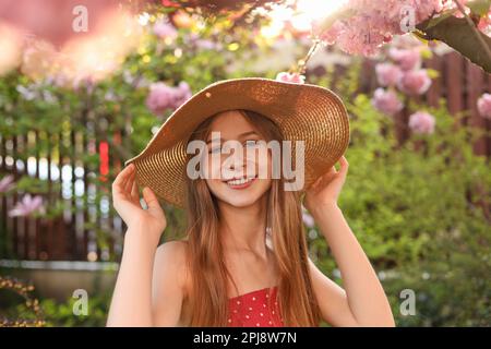 Beautiful teenage girl near blossoming sakura tree in park on sunny day Stock Photo