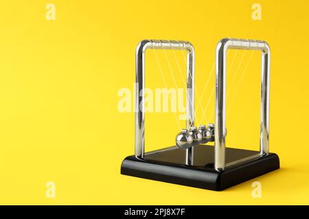 Newton's cradle on yellow background, space for text. Physics law of energy conservation Stock Photo