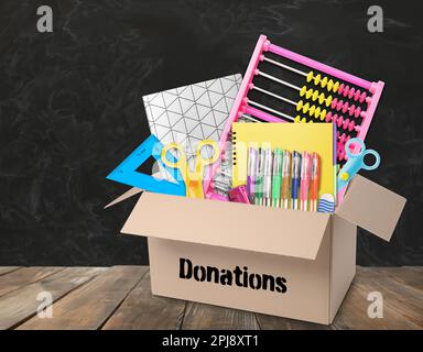 Donation box with different school stationery on wooden table near blackboard Stock Photo